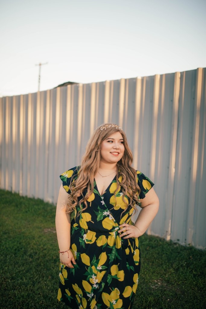Narda wearing a midi dress with lemons on it posing in front of a white fence at sunset