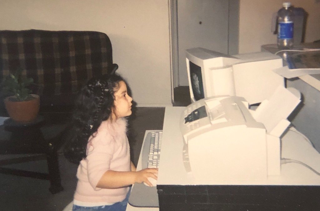 Young girl sitting at a computer from the nineties, touching the mouse